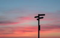 A street sign is silhouetted in black in the bottom right of the photo against a sunset sky in the background.